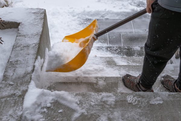 Individual is clearing snow from outdoor steps during a snowstorm, highlighting winter conditions and the physical effort involved in snow removal